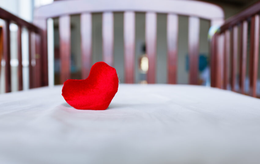 Red heart-shaped cushion on white crib bedding in a nursery.